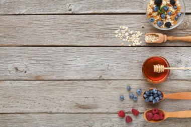 Farklı meyveler, bal ve yulaflar ahşap bir yüzeye konur. Sahne sağlıklı bir kahvaltı seçimi öneriyor. Her parça kolay servis için kâselere ya da kaşıklara konur..