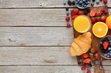 Çilek, yaban mersini ve böğürtlen içeren taze meyve koleksiyonu ahşap bir masa üzerine kurulmuştur. Anlaşmaya bir kruvasan ve bir bardak portakal suyu da dahil..