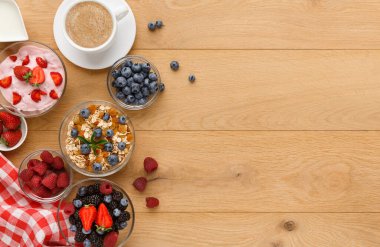 Kolaj, ahşap bir masada farklı kahvaltılık gıdalar gösterir. Kâselerde yoğurt, böğürtlen ve granola bulunurken bir fincan kahve yakınlarda duruyor. Kareli bir kumaş olay yerine detay ekler.
