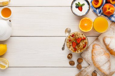 Kahvaltı malzemelerinin bir koleksiyonu ahşap bir masada düzenlenir. Çay, meyve, yoğurt, meyve suyu ve hamur işleri mevcut. Dekor, yemek için mükemmel bir sabah sahnesi gösteriyor..