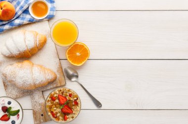 İçinde iki kruvasan, bir kase yoğurt, portakal dilimleri ve bir bardak meyve suyu bulunan kahvaltı malzemeleri. Sahne taze yiyecekleri gösteriyor..