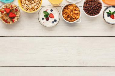 Farklı kahvaltı öğeleriyle dolu bir kase seti ahşap bir masada sergilenir. Koleksiyonda mısır gevreği, meyve ve çeşitli malzemelerle yoğurt yer alıyor..