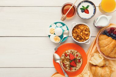 Farklı kahvaltılık yiyecekler masaya konur. Mısır gevreği, yoğurt, meyve ve içecek var. Her öge, sabah yemeği düzenine renk ve çeşitlilik ekler.