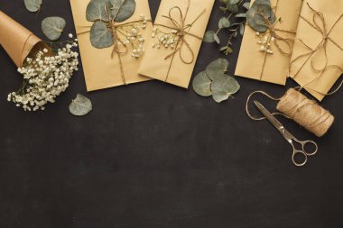 Paketlenmiş hediyeler, karanlık bir yüzeyde çiçekler ve yapraklarla düzenlenir. Makas ve sicim yakınlarda. Sahne, özel bir olay ya da olay için hazırlanan öğeleri gösterir.