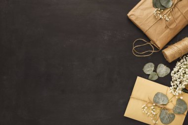 Kahverengi ve sarı kağıtlı paketlenmiş hediyeler koyu bir yüzeye yerleştirilir. Hediyelere dekoratif sicim ve kurumuş yapraklar eşlik ediyor. Bu sahne kutlamalar ve toplantılar için samimi bir his yaratıyor..