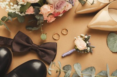 Bir düğün eşyası koleksiyonu kahverengi bir yüzeyde düzenlenir. Çiçekler, alyanslar, ayakkabılar ve papyon var. Kutlamanın detaylarını göstermek için her unsur dikkatlice yerleştirilir..