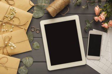 Bir zarf koleksiyonu sicimle bağlanmış, iPad ve ahşap masaya yerleştirilmiş bir akıllı telefon. Yakınlarda çiçekler, yüzükler ve bir makara ip var. Bu, planlama için bir çalışma alanı gösterir.