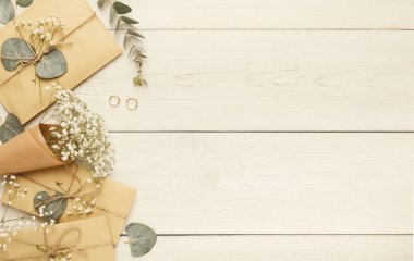 Tahta bir masaya iplerle bağlanmış bir zarf seti. Küçük beyaz çiçekler ve yüzükler yakınlarda. Yeşil yapraklar anlaşmayı tamamlıyor. Bu özel bir durum için uygun..