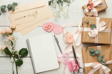 El yapımı eşyalar, paketlenmiş hediyeler, çiçekler, kurdeleler ve kırtasiye malzemeleriyle ahşap bir masada düzenlenir. Kurulum, özel bir durum için yaratıcı bir aktivite gösteriyor..