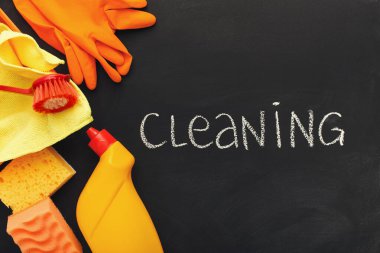 Bir temizlik malzemesi koleksiyonu karanlık bir yüzeyde sergilenir. Eldivenler, süngerler, fırça, bez ve bir şişe temizlik solüsyonu var. Temizlik kelimesi tebeşirle yazılmış..
