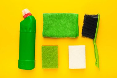 Sarı arka planda bir temizlik aletleri koleksiyonu düzenlenir. Aletler arasında bir şişe temizleyici, sünger ve bir fırça var. Her parça kolayca görülebilir ve ulaşılabilir..