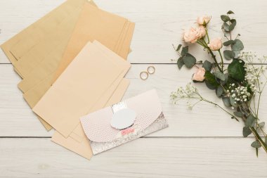 Çeşitli kağıt çarşaflar ve tahta bir masanın üzerine yerleştirilmiş bir zarf. Yakınlarda çiçek elementleri ve halkaları var. Bu da zanaat ya da planlama faaliyeti olduğunu gösteriyor..