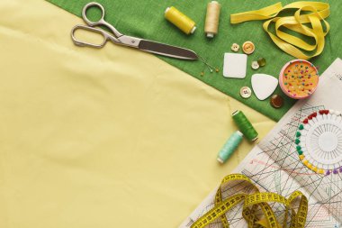 Masada, dikiş malzemelerinin bir koleksiyonu var. Makas, iplik, düğme ve renk çarkı düzgünce düzenlenmiş. Ölçüm bandı kağıt ve iğne yastığının yanında yatıyor.