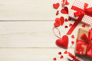 Kırmızı ve beyaz kağıda sarılı birkaç hediye hafif bir ahşap masada oturur. Kalp süslemeleri ve konfetiler hediyelerin etrafını sararak, kutlama veya etkinlik için şenlikli bir ortam yaratıyor..