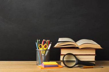 Kalem ve kalemlerle dolu bir fincanın yanındaki tahta masada bir kitap seti duruyor. Yakınlarda bir büyüteç duruyor, yapışkan notlar etrafa saçılmış..