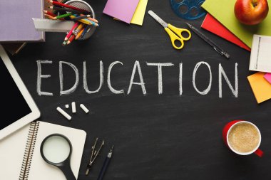 Bir masa makas, bir defter, renkli kağıtlar ve bir kahve fincanı gibi çeşitli okul malzemeleriyle doludur. Eğitim kelimesi siyah bir yüzeye tebeşirle yazılmıştır..