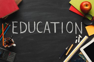 Siyah bir yüzeye yerleştirilmiş bir okul malzemeleri koleksiyonu eğitim kelimesine odaklanmaktadır. Ögeler arasında kitaplar, kalemler, bir elma ve bir tablet, öğrenim ve öğrenim için canlı bir ortam yaratmak yer alıyor..