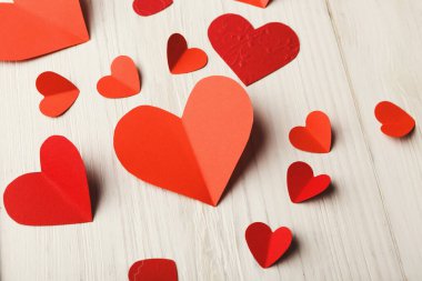 Tahta bir yüzeye yayılmış farklı boyutlarda ve şekillerde bir sürü kağıt kalp var. Kalpler kırmızı ve pembenin gölgesinde basit bir dekoratif ekran oluşturuyor..