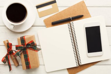 A collection of office supplies shows a cup of coffee, an open notepad, a pen, a phone, and a gift box. The setting includes a simple wooden table and a card placed on the side.