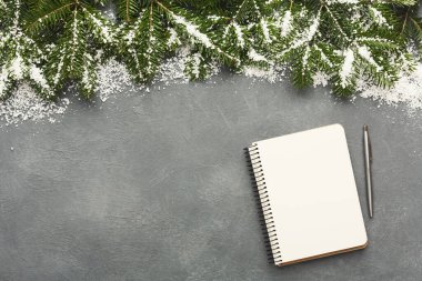 A collage shows a gray surface adorned with snow, greenery, and a blank notebook with a pen. This setting suggests planning or creativity during the winter season.