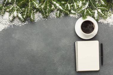 A winter scene shows a cup of coffee on a white saucer. A blank notebook and pen sit next to it. Pine branches covered in snow frame the top of the grey background.