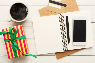 Masadaki eşyalardan oluşan bir koleksiyonda bir kurdele, bir defter, bir kalem, bir akıllı telefon ve bir fincan kahve ile paketlenmiş bir hediye gösteriliyor. Olay yeri basit ve günlük görevler için düzenlenmiş..