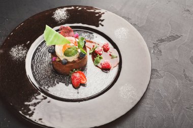 Tatlılar siyah bir tabakta sıralanır. Sergide, üzerinde meyve ve nane olan yuvarlak çikolatalı bir tatlı yer alıyor. Ana yemeğin etrafına farklı böğürtlenler konur..