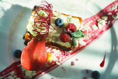 Tatlılardan oluşan bir koleksiyon bir tabakta düzenlenir. Böğürtlen ve ahududu gibi çeşitli meyveler en üste konur. Kırmızı sos ve diğer malzemeler tabağın tasarımını güçlendirir..