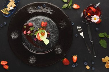 Tatlı eşyalar taze meyve ve içeceğin yanında siyah bir tabakta hazırlanır. Ekranda çeşitli renkler ve dokular var. Ayarlama yiyeceklerin detaylarını vurguluyor.