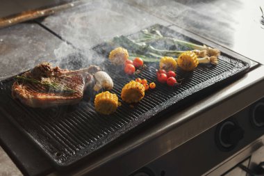 Bir ızgara et, mısır, soğan ve domatesle doludur. Aşçı, ızgara ısınırken yemek hazırlar..