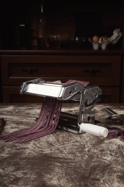 Ev yapımı fettuccine makarna makine üzerinde Siyah frenk üzümü ile hazırlanıyor. Kesme çiğ mor hamur tagliatelle özel ekipman, geleneksel İtalyan mutfağı kavramı, kopya alanı içine