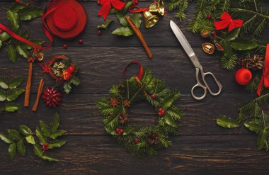 Mevsimlik çelenk yapımı ahşap bir masada yapılır. Yeşillik, kurdeleler, süsler ve aletler ayarlandı. Makas ve süslemeler doğal eşyalarla şenlikli bir çelenk yapmak için kullanılır..