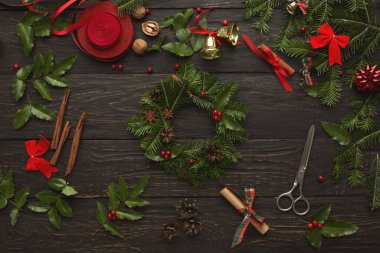 Farklı yeşillikler, kurdeleler ve dekorasyonlar koyu ahşap bir yüzeye yerleştirilmiştir. Eşyalar arasında çanlar, yaylar ve kozalaklar var. Bunlar tatil zanaatı yapmak için kullanılır..