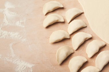 Hamur köfteleri ahşap bir yüzeye dizilir ve un etrafa saçılır. Hamur köftelerinin yanında düzleşir. Sahne yemek hazırlığı öneriyor..