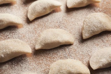 Hamur köfteleri ahşap bir yüzeyde düzgün sıralara konur, hafifçe un ile toz alınır. Hamur küçük yarım ay şeklinde, pişirmeye hazır..