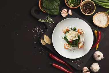 Taze malzemeler bir tabak salatanın etrafına dizilir. Sebzeler ve bitkiler siyah bir kesme tahtasına konur. Sarımsak, acı biber ve baharatlar yemekte kullanıma hazır..