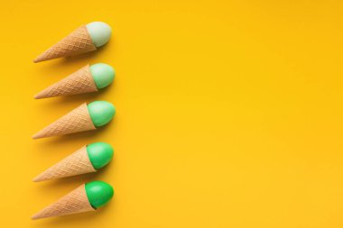 Parlak Paskalya geçmişi. Kreatif dondurmalar yeşil renkli yumurtalar ile Waffle konileri sarı arka plan, üst görünüm, boşluk kopyala