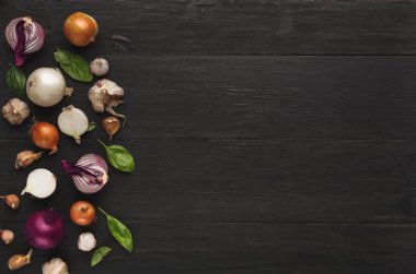 Çeşitli sebzelerden oluşan bir kolaj koyu ahşap bir yüzeye yayılır. Kırmızı, beyaz ve sarı soğanlar sarımsak ve yeşil yapraklarla karışıyor..