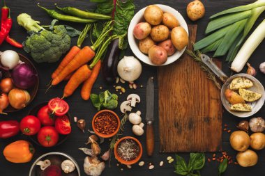 Taze sebze ve otlardan oluşan bir koleksiyon koyu ahşap bir masanın üzerine yerleştirilir. Renkli ürünler arasında biber, havuç, soğan ve daha fazlası vardır. Kesme tahtası ve bıçak da var..