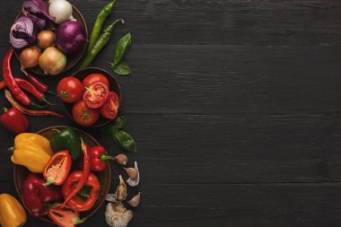 Ahşap kaselerde biber, domates ve baharat içeren bir sebze koleksiyonu gösteriliyor. Kurulum koyu ahşap bir masada, yemek ve yemek hazırlığı için hazır..