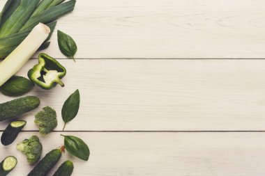 Çeşitli taze sebze koleksiyonu ahşap bir masada sergilenir. Sebzeler arasında pırasa, salatalık, yeşil dolma biber, fesleğen yaprağı ve brokoli yer alıyor..