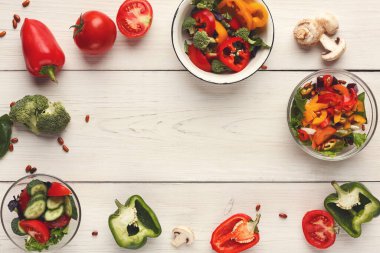 Taze sebzeler ahşap bir masanın üzerindeki kaselere konur. Çeşitli türde biber, domates ve brokoli görülebilir. Sahne yemek hazırlama ya da salata yapma için hazırlanmayı temsil ediyor..