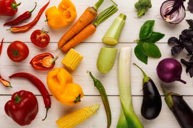 Bir grup taze sebze ahşap bir yüzeye serilir. Koleksiyonda çeşitli renk ve şekilleri gösteren biber, domates, havuç, mısır, kabak ve brokoli yer alıyor..