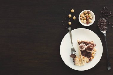 Koyu ahşap bir masanın üzerine bir tatlı seti konur. Beyaz bir tabakta ceviz ve çikolatalarla çevrili bir dilim pasta var. Pastanın yanında bir çatal duruyor..