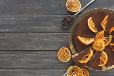 Üzerinde portakal dilimleri olan yuvarlak bir pasta seti. Kek parçaları kesilip ahşap bir masaya konur. Tatlıyı çevreleyen dekoratif kuru portakallar ve çikolata parçaları..