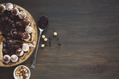 Kolaj krema ve çikolatayla kaplı yuvarlak bir pasta gösteriyor. Yanında bir kase karışık fındık ve bir kaşık kahve çekirdeği var. Bu kurulum bir tatlı teması gösterir.