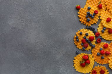 Waffle 'lar gri bir yüzeye serpilmiş taze ahududu ve yaban mersinleri ile çevrelenmiştir. Yemekler, waffle 'ların arasına meyve karıştırılmış sıradan bir şekilde düzenlenir..