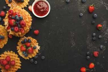 Karanlık bir yüzeye bir waffle seti yerleştirilir. Taze çilekler ve yabanmersinleri etrafa saçılmış. Yanında küçük bir kase reçel duruyor, ekrana ekliyor..