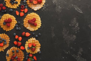 Taze böğürtlenli waffle koleksiyonu. Çilek, yabanmersini ve ahududu her yere yayılmış. Bu sahne karanlık bir yüzeye kurulmuş ve kahvaltının özünü yakalıyor..