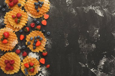 Yuvarlak waffle seçimleri karanlık bir yüzeye göre düzenlenir. Her waffle taze çilek, yabanmersini ve ahududu ile kaplıdır. Düzen renk ve dokuların bir karışımını gösterir.